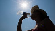 Frau mit Sonnenhut trinkt aus einer Wasserflasche.