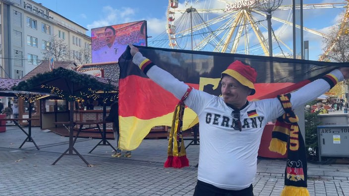 Ein Fan der deutschen Nationalmannschaft hält stolz eine Flagge auf einem Weihnachtsmarkt empor.