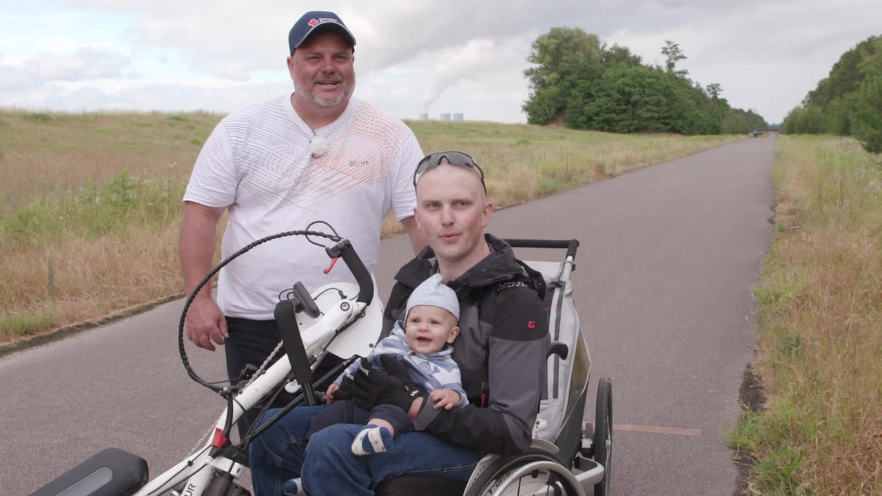Ersthelfer Henryk Menzel und Daniel Mauell im Rollstuhl mit Baby auf dem Schoß