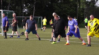 Übergewichtige Fußballspieler bei Dehnübungen auf dem Sportplatz