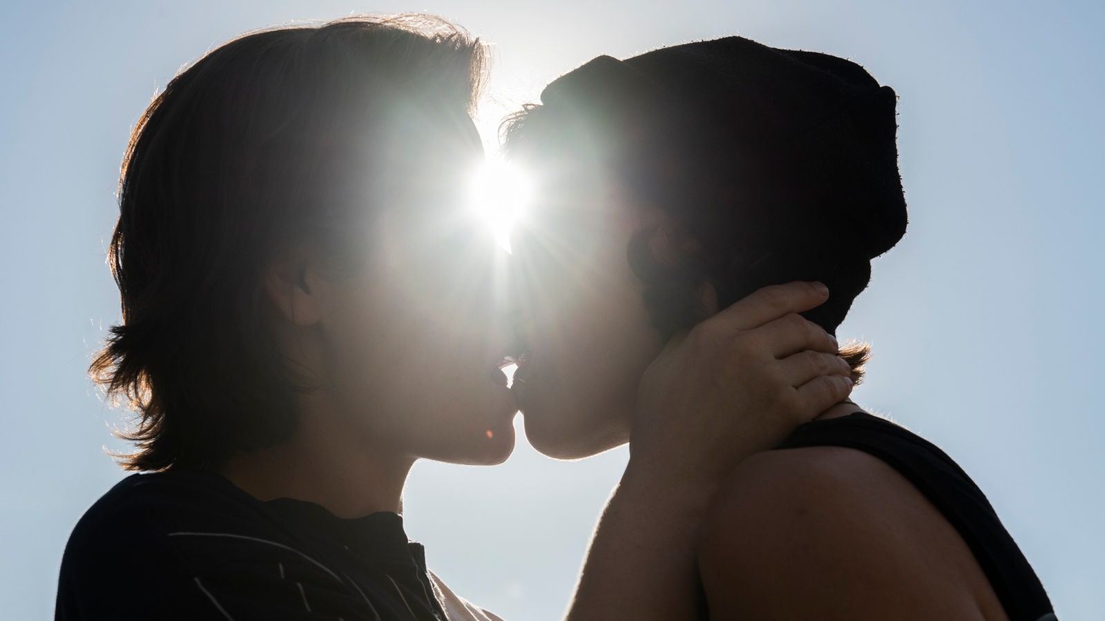 Zwei Frauen küssen sich, ein heller Sonnenstrahl leuchtet auf ihre Gesichter.