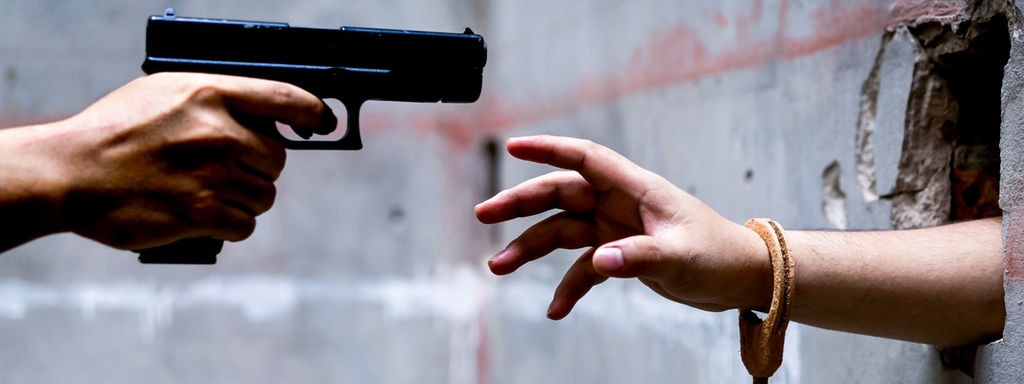 Waffe gerichtet auf eine Hand, die aus einer Wand ragt.