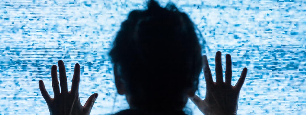 Eine Frau drückt sich nah an einen Fernsehbildschirm mit Störbild.