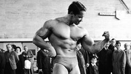 Arnold Schwarzenegger post 1976 in Unterhose vor einer beeindruckten Menschenmenge.