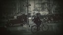 Schwarz-weiß Bild: Ein Fahrradfahrer schaut auf einen Polizisten in den Straßen Berlins der 1930er, um sie herum Autos. 