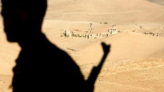 Der Schatten eines bewaffneten Soldaten vor Wüste in Afghanistan.
