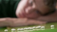 Antidepressiva: Ein junger Mann schaut auf Pillen, die vor ihm liegen. 