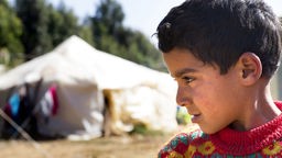 Ein Flüchtlingskind, im Hintergrund eine Zeltunterkunft