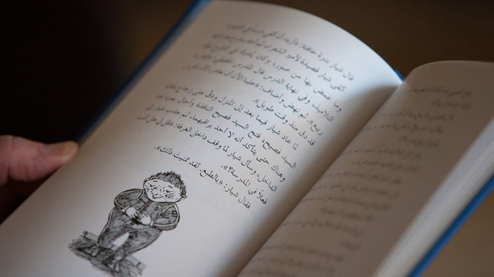 Ein aufgeschlagenes Buch mit arabischer Schrift und einer Zeichnung von dem "Sams".