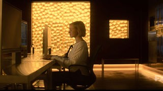 Screenshot: "Devs" - Mitarbeiterin der Devs Abteilungs vor dem Rechner sitzend. 