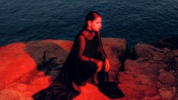 Sofia Kourtesis: "Madres" - die Sängerin am Saum eines Sees sitzend im Abendlicht. 