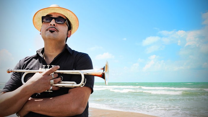 Roy Paci steht mit Trompete am Strand