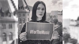 DJ Rebekah mit einem Schild auf dem der Hashtag ForTheMusic steht