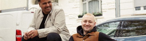 Das Produzenten-Duo Indialman auf einer Bank an einer Straße sitzend