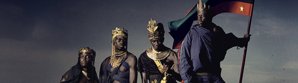 Cover des Albums "Afrikan Alien" von Pa Salieu: Vier Schwarze Personen in dunklen Tüchern gekleidet und mit goldenem Schmuck behangen; die vordere Person hält eine Flagge