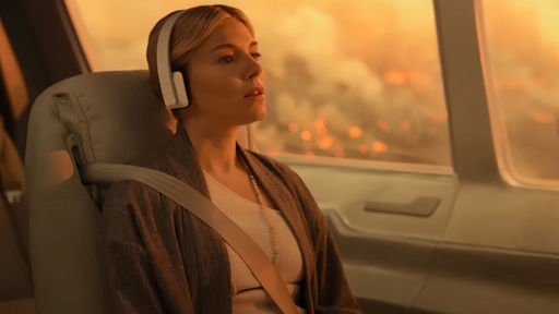 "Extrapolations" - Sienna Miller sitzt angeschnallt in einem Flugzeug. durch das Fenster sieht man riesige brennende Flächen. 