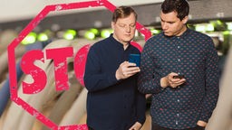 COSMO Tech- Netzsperren. Jörg Schieb und Dennis Horn schauen auf ihre Handys. Im Hintergrund der Schriftzug "STOP"