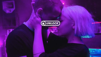 Ein junges Paar (Mann & Frau) umarmen sich innig im bunten Licht eines Clubs. 
