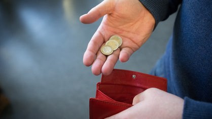 Eine Person hält in einer Hand fünf Euro in Münzen, in der anderen ein leeres Portmonaie