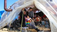 Frau mit Kindern sitzt im Erdbebengebiet Hatay in einem Zelt