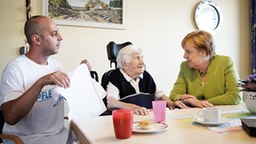 Bundeskanzlerin Angela Merkel mit Pfleger Ferdi Cebi bei einer Bewohnerin des Johannisstift