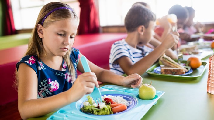 Kinder sitzen in der Schulkantine am Tisch und essen