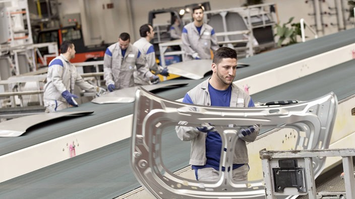 Produktion des Golf 7 in Wolfsburg, ein Mitarbeiter nimmt ein Teil einer Motorhaube nach dem Pressvorgang vom Transportband