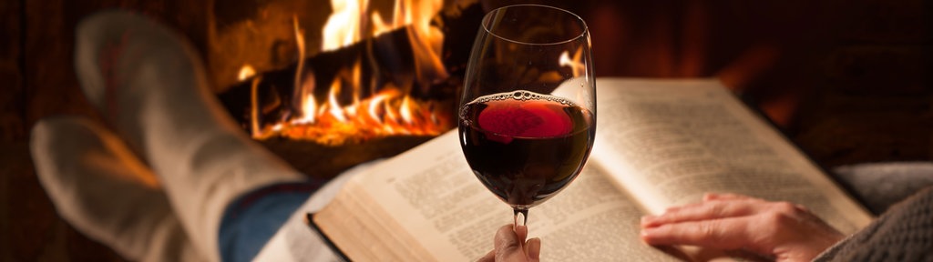 Frau am Kamin mit einem Buch und Rotwein