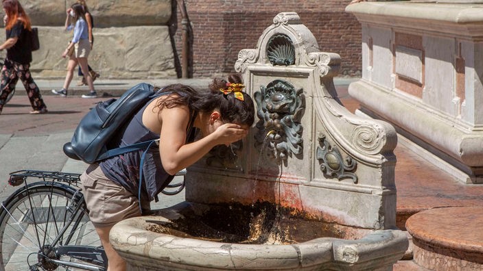 Una ragazza si rinfresca sotto una fontanella