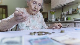 Eine alte Frau schaut auf Geldscheine und Münzen