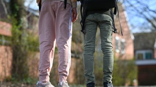 Beine von Jugendlichen von hinten fotografiert. Rosa Jogginghose und grüne Jeans