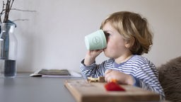 Ein Kind trinkt aus einem Plastikbecher am Esstisch