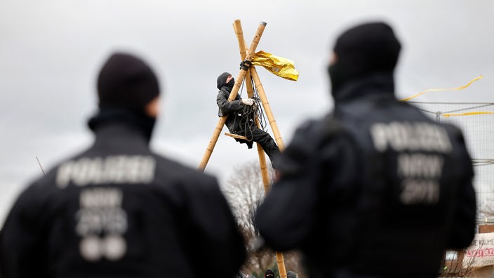 Poliziotti sorvegliano un attivista arrampicato su dei pali