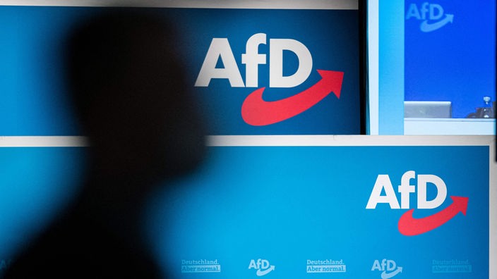 Silueta čoveka koji prolazi ispred panoa na kome je logo AfD-a