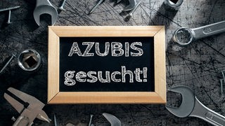 Natpis "Traže se azubis" na tabli koja se nalazi među alatom na radnom stolu