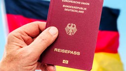 Ruka drži nemački pasoš, u pozadini nemačka zastava