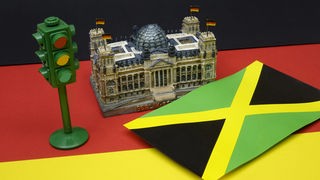 Neben einem Reichstag steht eine Ampel und liegt eine Fahne von Jamaika