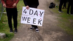 Dva čoveka na protestima, jedan nosi transparent "4 Day Week"