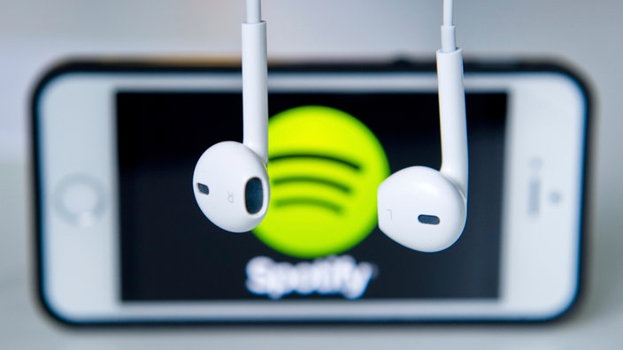 Slušalice vise ispred smartfona na kome je logo aplikacije Spotify