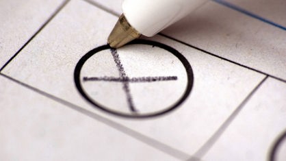 glasački listić i olovka koja upisuje krstić u krug