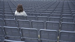 Žena snimljena s leđa sedi sama među redovima praznih sedišta