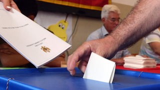Ruka ubacuje listić u glasačku kutiju, u pozadini zastava Crne Gore