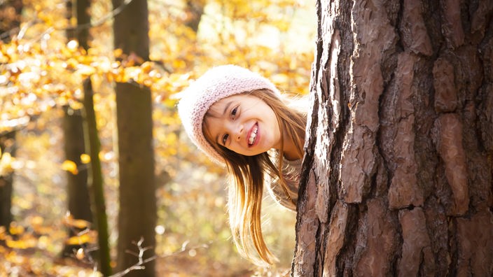 Devojčica izviruje iza drveta u igri žmurke