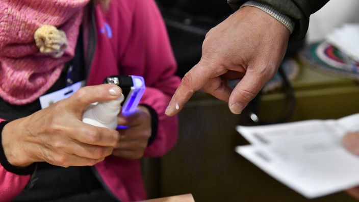 Pripadnica komisije na izbornom mestu prska sprej na prst birača
