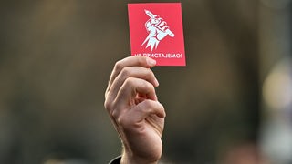 Ruka drži crveni karton sa stilizovanom pesnicom koja drži olovku i natpisom "Ne pristajemo!"