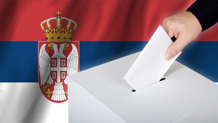 Ruka ubacuje listić u glasačku kutiju; u pozadini zastava Srbije