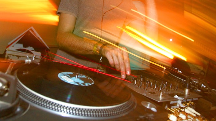 Ein DJ steht in einem Club hinter den Plattentellern