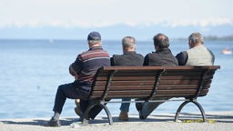 Vier Herren fortgeschrittenen Alters sitzen in Konstanz auf einer Bank am Ufer und blicken auf den Bodensee hinaus