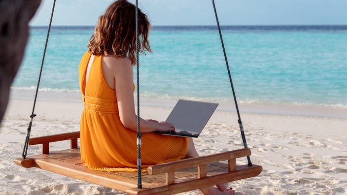 Devojka na ljuljašci radi na laptopu na plaži