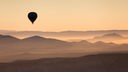 Ein Heißluftballon schwebt über einem Gebirge im Sonnenuntergang